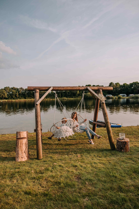 Kvinde og barn sidder på hængestolsgynge ved søen i Recreatiepark De Achterste Hoef, Holland.