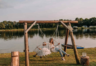 Woman and child relax on hanging swing chairs by the lake at Recreatiepark De Achterste Hoef, Netherlands.