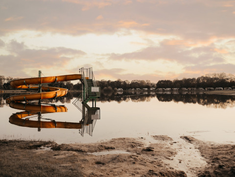 Tobogán amarillo reflejado en el lago tranquilo de Recreatiepark De Achterste Hoef al atardecer, Países Bajos.