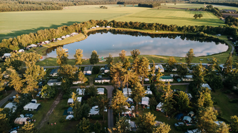 Aerial view of De Achterste Hoef holiday park with caravans, trees, and a lake in North Brabant, Netherlands.