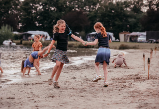 Børn leger på sandstranden ved en sø i Recreatiepark De Achterste Hoef, feriepark i Nord-Brabant.