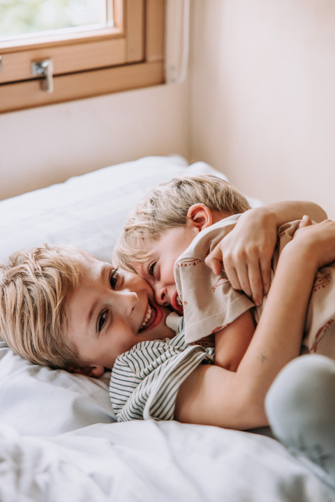 Dos niños felices se abrazan y sonríen juntos en una cama en una habitación acogedora de Recreatiepark De Achterste Hoef.