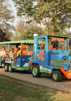 El tren Zoef Express lleva a familias por el parque vacacional De Achterste Hoef rodeado de vegetación.