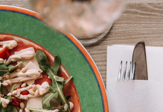 Insalata con pinoli e condimento accanto a una bevanda e tovagliolo di De Achterste Hoef.
