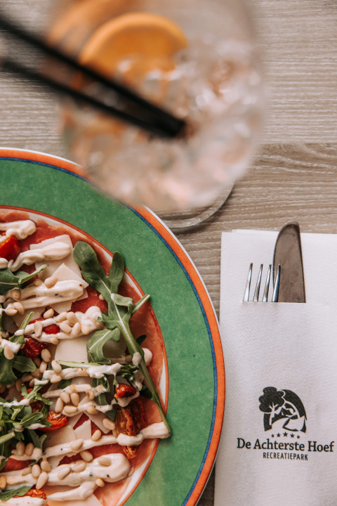 Salade met pijnboompitten en dressing, met een drankje en servet van Recreatiepark De Achterste Hoef.