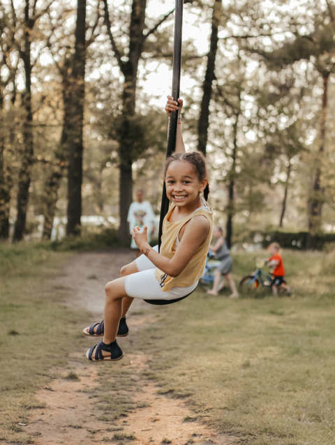 Una niña sonriente se desliza en una tirolesa en Recreatiepark De Achterste Hoef, rodeada de árboles.