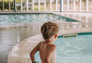Et barn sidder ved kanten af en indendørs swimmingpool i Recreatiepark De Achterste Hoef, Holland.