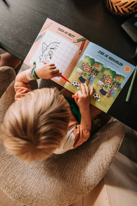 Child working with activity book at a table in Recreatiepark De Achterste Hoef, North Brabant, Netherlands.