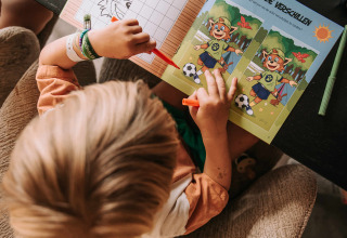 Bambino gioca con un libro di attività al tavolo al Recreatiepark De Achterste Hoef, Brabante Settentrionale, Paesi Bassi.