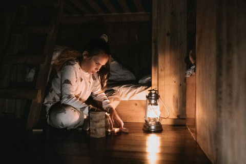 Bambina gioca con blocchi di legno vicino a una lanterna in una baita al Feather Down Botterheerd, Groningen.