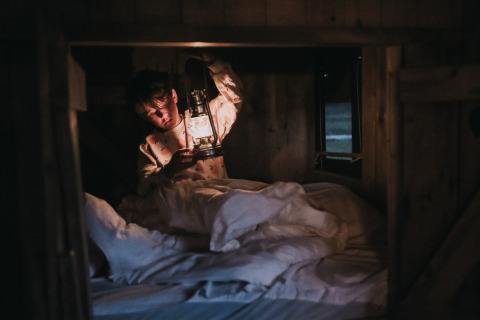 Bambino con lanterna seduto in un letto di legno al Feather Down Botterheerd, parco vacanze a Groningen, Paesi Bassi.