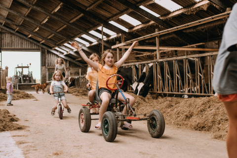 Kinder fahren mit Kettcars und Fahrrädern in einer Scheune bei Feather Down Botterheerd, Groningen, Niederlande.