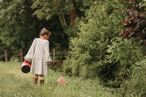Fille avec seau et ballon marchant dans un champ vert à Feather Down Botterheerd, Groningue, Pays-Bas