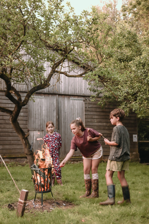 Drei Kinder rösten Marshmallows über offenem Feuer im Garten bei Feather Down Botterheerd, Groningen.