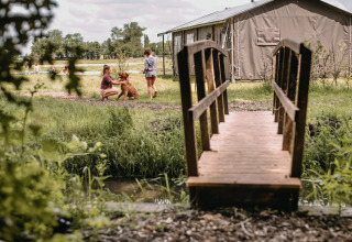 Bambini che giocano con un cane vicino a un ponte di legno al Feather Down Botterheerd, parco vacanze a Groningen.