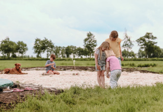 Kinder spielen im Sandkasten mit einem Hund auf dem Feather Down Botterheerd Ferienpark in Groningen, Niederlande.