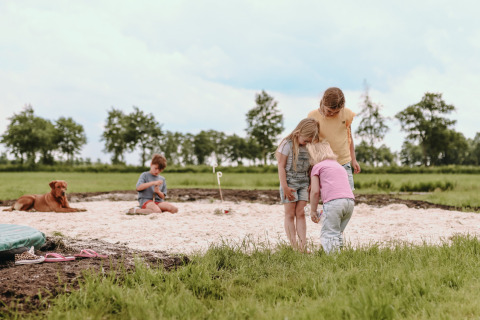 Niños juegan en un arenero con un perro cerca en Feather Down Botterheerd, parque vacacional en Groningen, Países Bajos.