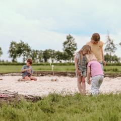 Niños juegan en un arenero con un perro cerca en Feather Down Botterheerd, parque vacacional en Groningen, Países Bajos.