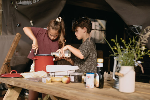 Dos niños cocinan juntos al aire libre en una mesa de madera en Feather Down Botterheerd, Groningen, Países Bajos.