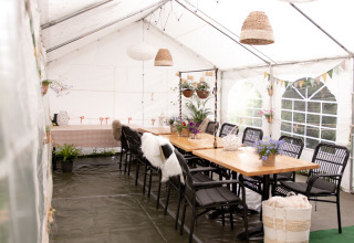 Interno di tenda accogliente con tavoli e sedie presso Feather Down Botterheerd, parco vacanze a Groningen.