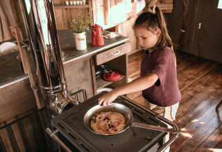 Un bambino cucina su una stufa in una baita rustica al parco vacanze Feather Down Botterheerd a Groningen, Paesi Bassi.