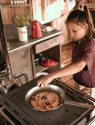 Et barn laver mad på et komfur i en rustik hytte ved Feather Down Botterheerd feriepark i Groningen.