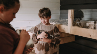 Dos niños juegan con cobayas en un acogedor establo del parque vacacional Feather Down Botterheerd en Groningen.