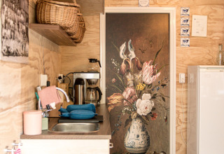 Small wooden kitchen with basket, coffee maker, and floral door mural at Feather Down Botterheerd, Groningen.