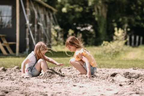 Two girls play in the sand at Feather Down Botterheerd holiday park in Groningen, Netherlands, outdoors.