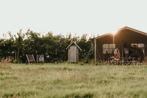 Safari teltet Tent house med privat udendørs bruser, solnedgang, grøn eng og afslappede besøgende.