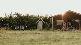 Safari-Zelt Tent house mit privater Dusche im Freien, Abendsonne und Menschen, die sich entspannen.