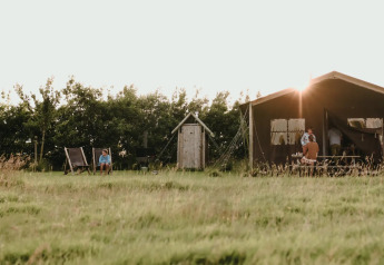 Safari teltet Tent house med privat udendørs bruser, solnedgang, grøn eng og afslappede besøgende.