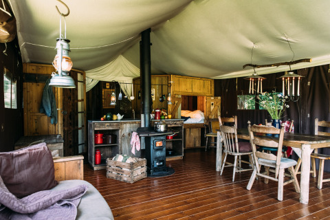 Interior de una tienda safari acogedora con estufa de leña, mesa de comedor, cocina y muebles rústicos.