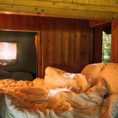 Knusse slaaphoek in een safaritenthuis met houten wanden, daglicht en comfortabele lakens.