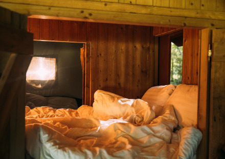 Knusse slaaphoek in een safaritenthuis met houten wanden, daglicht en comfortabele lakens.