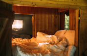 Accogliente angolo letto in tenda safari con pareti in legno, luce naturale e morbida biancheria.