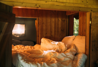 Cozy sleeping nook in a safari tent house with private hot shower, wood paneling, and soft bedding.