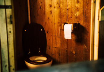Badeværelse med trævægge, toilet og toiletpapir inde i et safaritelt med privat bruser ved siden af teltet.