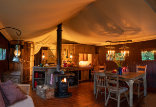 Interior de tienda safari con iluminación cálida, estufa de leña, cocina rústica y mesa de comedor de madera.
