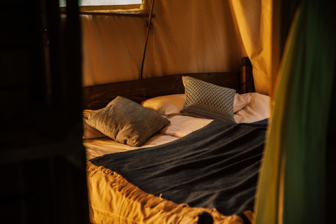 Cama acogedora dentro de la tienda safari Tent house, con ducha caliente privada junto al toldo.