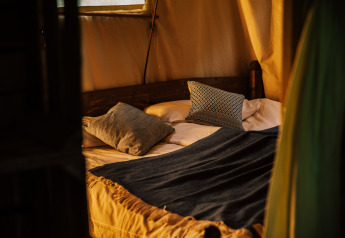 Cama acogedora dentro de la tienda safari Tent house, con ducha caliente privada junto al toldo.