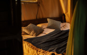 Cozy bed setup inside a safari tent named Tent house, featuring a private hot shower next to it.