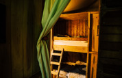 Lits superposés en bois et rideau dans une tente safari Tent house avec douche privée à côté.