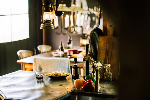 Interior rústico de tienda safari con mesa, verduras frescas, botellas de vino y luz cálida.
