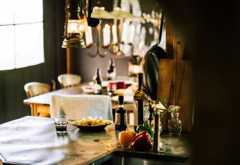Interior rústico de tienda safari con mesa, verduras frescas, botellas de vino y luz cálida.