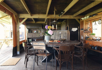 Binnenkant van een glamping-accommodatie met houten eettafel, gemixte stoelen en open keuken.
