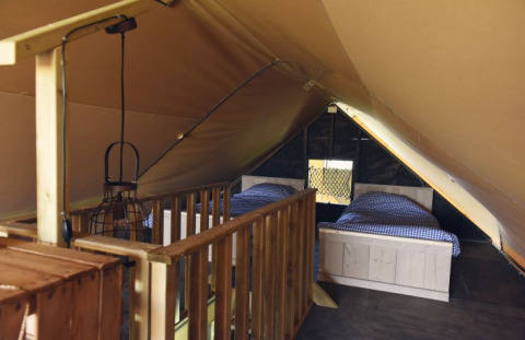 Interior view of a glamping accommodation with two single beds, wooden railing, and cozy lighting.