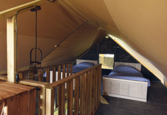 Vista interna di una tenda glamping con due letti singoli, corrimano in legno e luce accogliente.