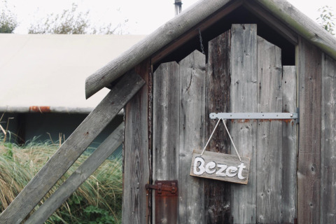 Porte en bois avec panneau 'Bezet' dans un hébergement glamping, avec tente et nature en arrière-plan.