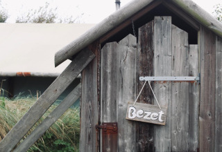 Porta di legno con cartello 'Bezet' presso un alloggio glamping, circondata da natura e una tenda.